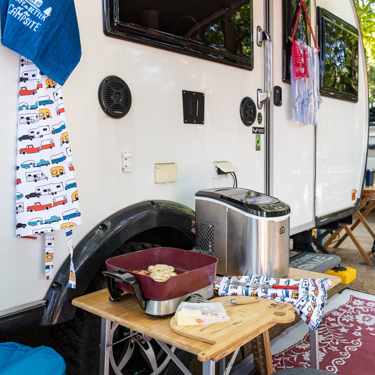 Campsite set up in front of camper trailer with table and airfryer and food being prepared